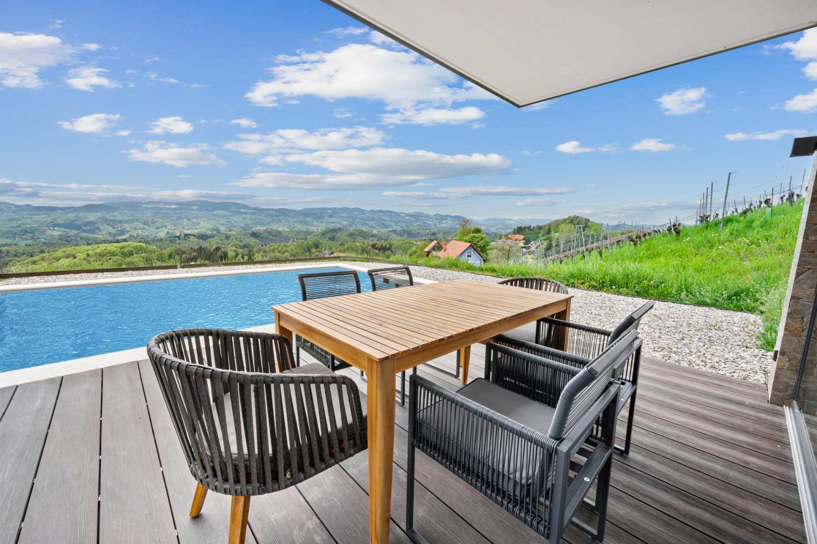 Gemütlicher Essbereich auf der Holzterrasse am Pool mit weitem Blick über die grüne Hügellandschaft.