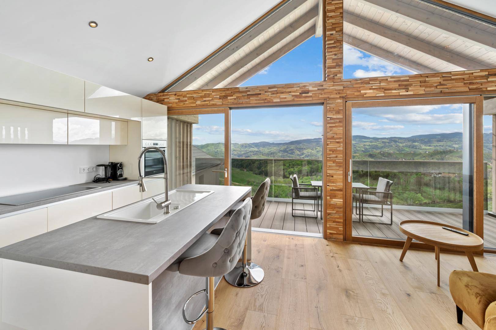 Moderne offene Küche mit Kochinsel und großen Glasfronten, die Zugang zu einem Balkon mit Panoramablick bieten.