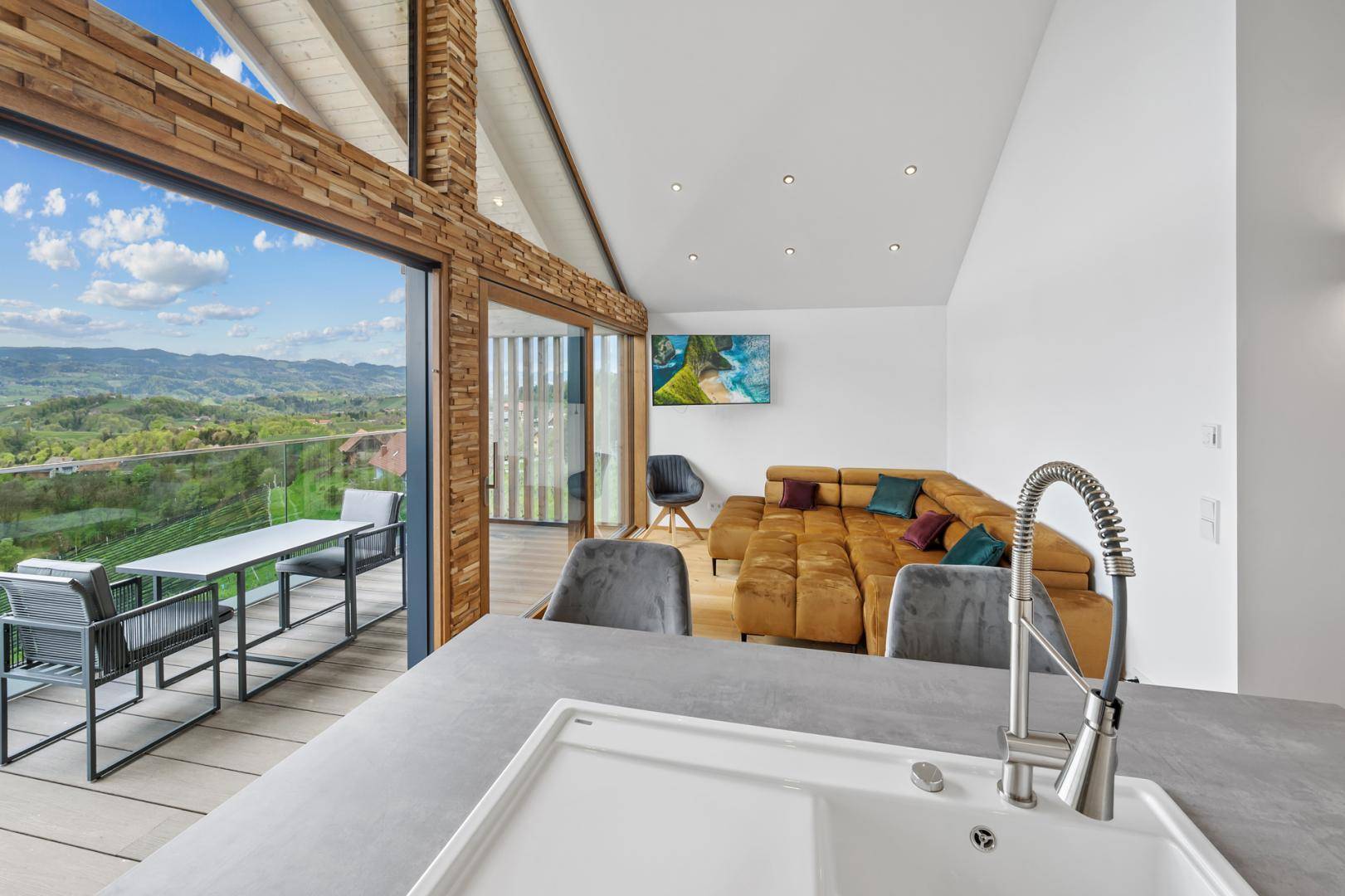 Offener Wohn- und Essbereich mit moderner Küche, Sofa und großen Fenstern mit Panoramablick.