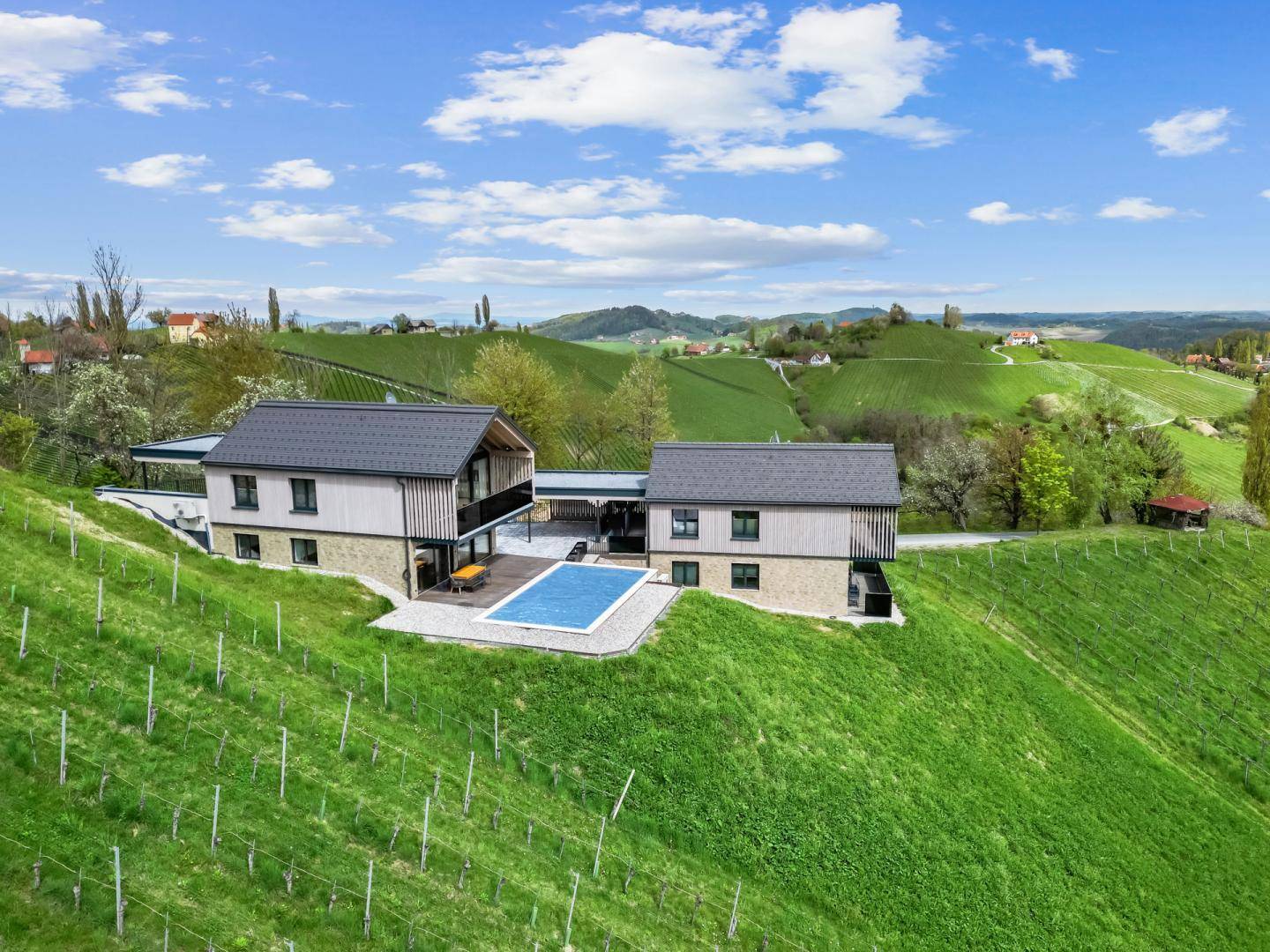 Luftaufnahme der beiden modernen Häuser mit Pool, eingebettet in die grüne Hügellandschaft und Weinberge.