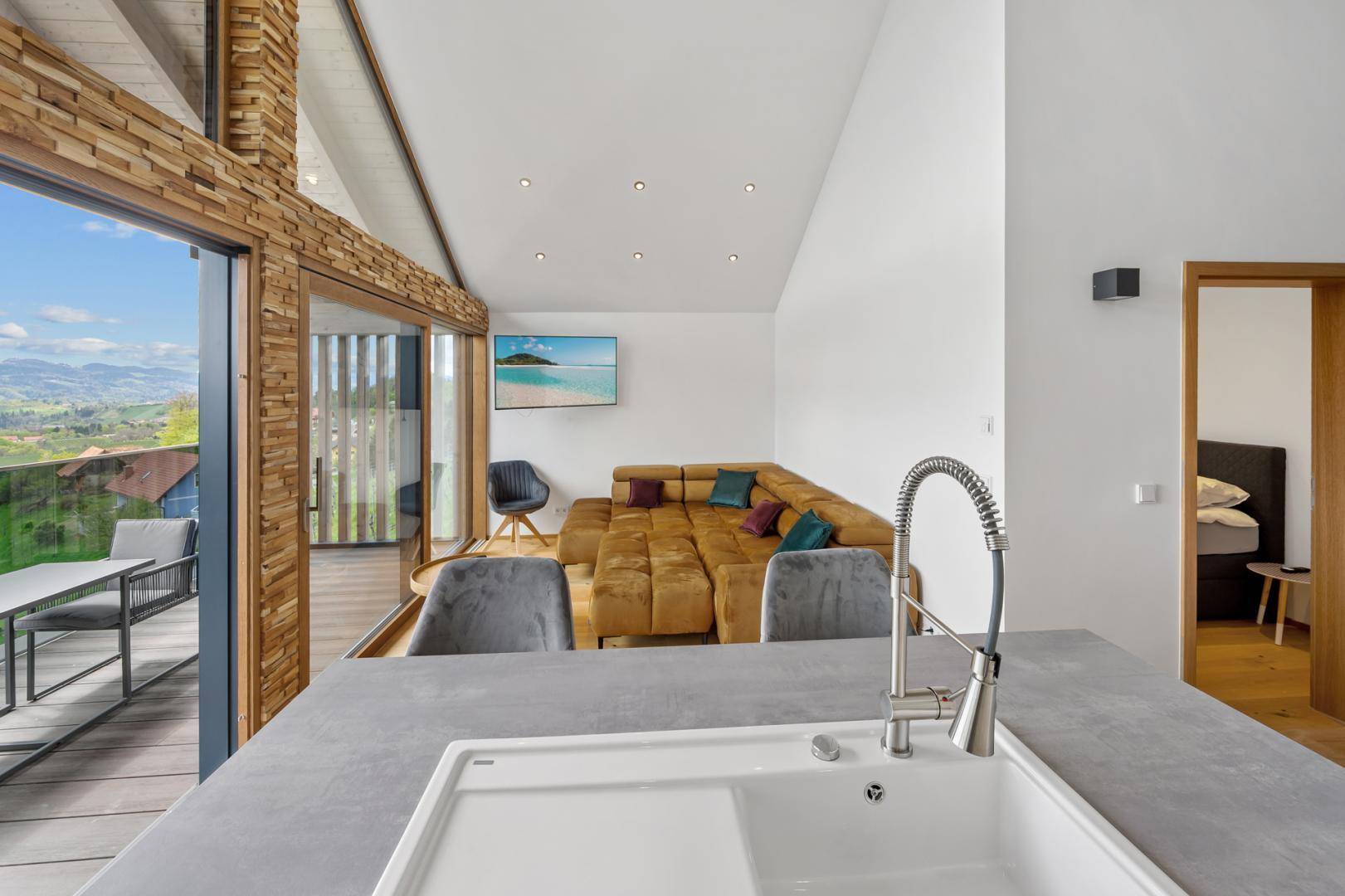 Offener Wohnbereich mit moderner Küche, bequemer Couch und Zugang zur Terrasse mit Panoramablick.