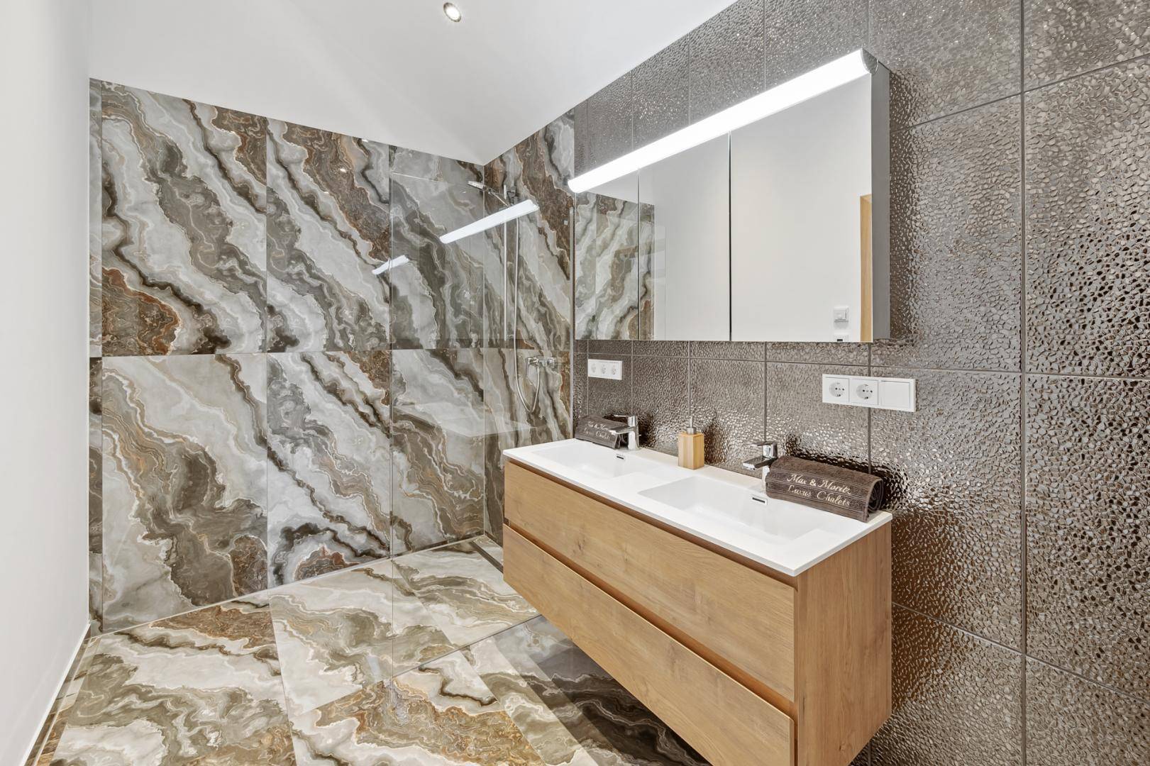 Modernes Badezimmer mit Doppelwaschbecken, großer Dusche und eleganten Marmorfliesen.