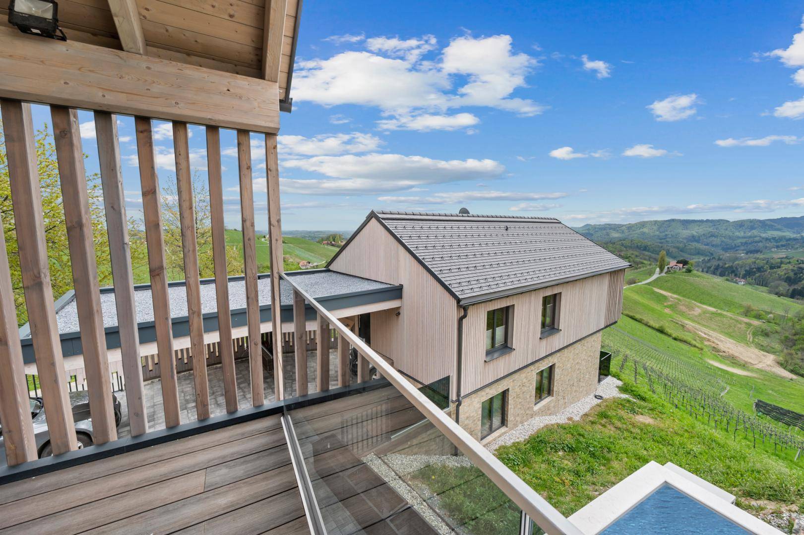 Panoramablick von einem Balkon auf das Nachbarhaus und die weitläufige grüne Hügellandschaft.