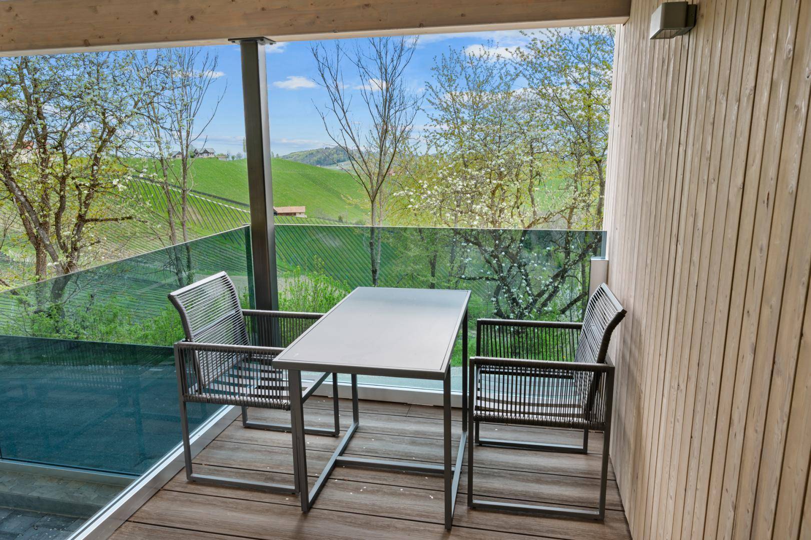 Kleiner Balkon mit Sitzgelegenheiten und weitem Blick auf die grüne Hügellandschaft und Bäume.
