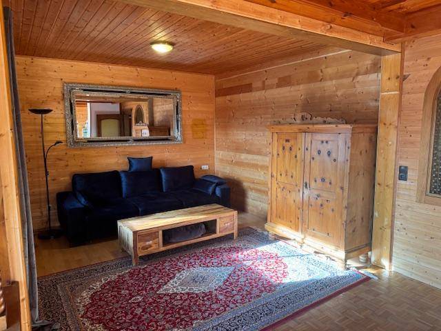 Rustikales Wohnzimmer mit Holzwänden, dunklem Sofa, traditionellem Holzschrank und Teppich.