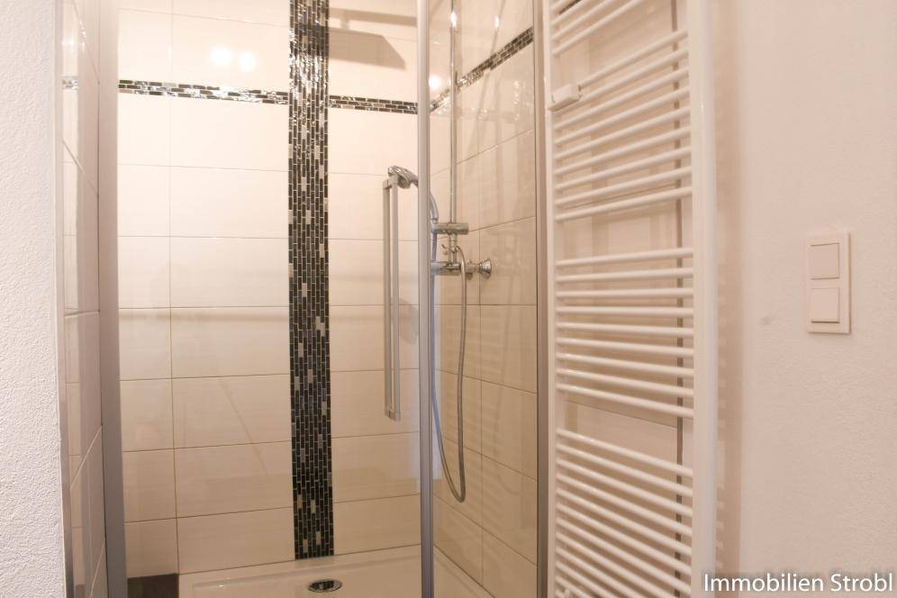 Modernes Badezimmer mit Duschkabine, weißen Fliesen und beheiztem Handtuchhalter.