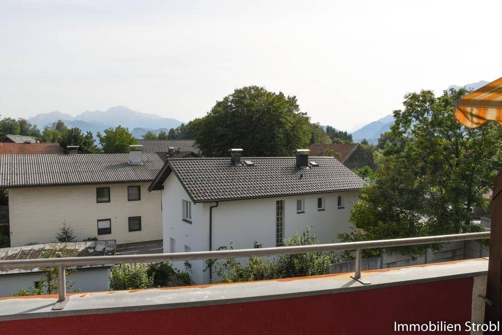 Balkon mit Blick auf umliegende Häuser und ferne Berge unter klarem Himmel.