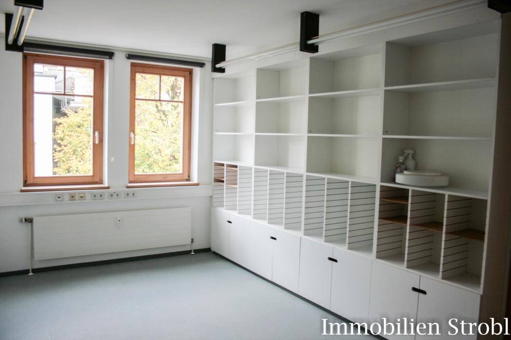 Geräumiger Büroraum mit integrierten weißen Regalsystemen und zwei großen Fenstern für viel Tageslicht.