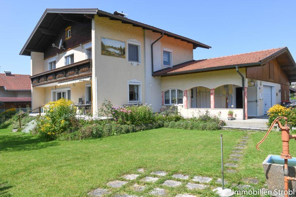 Traditionelles Haus mit gepflegtem Garten, Blumenbeeten und einer alten Wasserpumpe.
