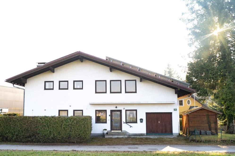 Weißes Einfamilienhaus mit Satteldach, Solaranlage, integrierter Garage und gepflegter Hecke.