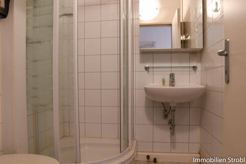 Badezimmer mit Duschkabine, Waschbecken und Spiegelschrank, komplett gefliest.