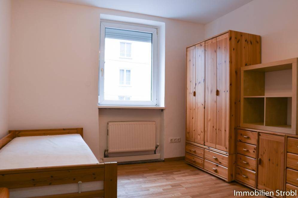 Schlafzimmer mit Holzbett, großem Kleiderschrank und Fenster für Tageslicht.