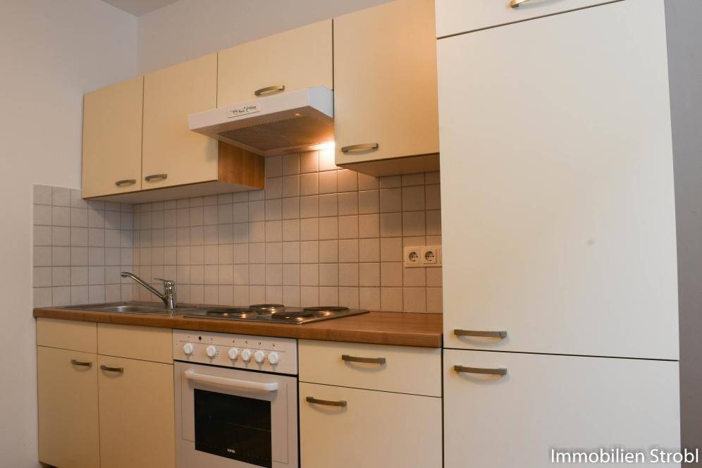 Funktionale Einbauküche mit Herd, Backofen und Spüle, umgeben von hellen Fliesen.