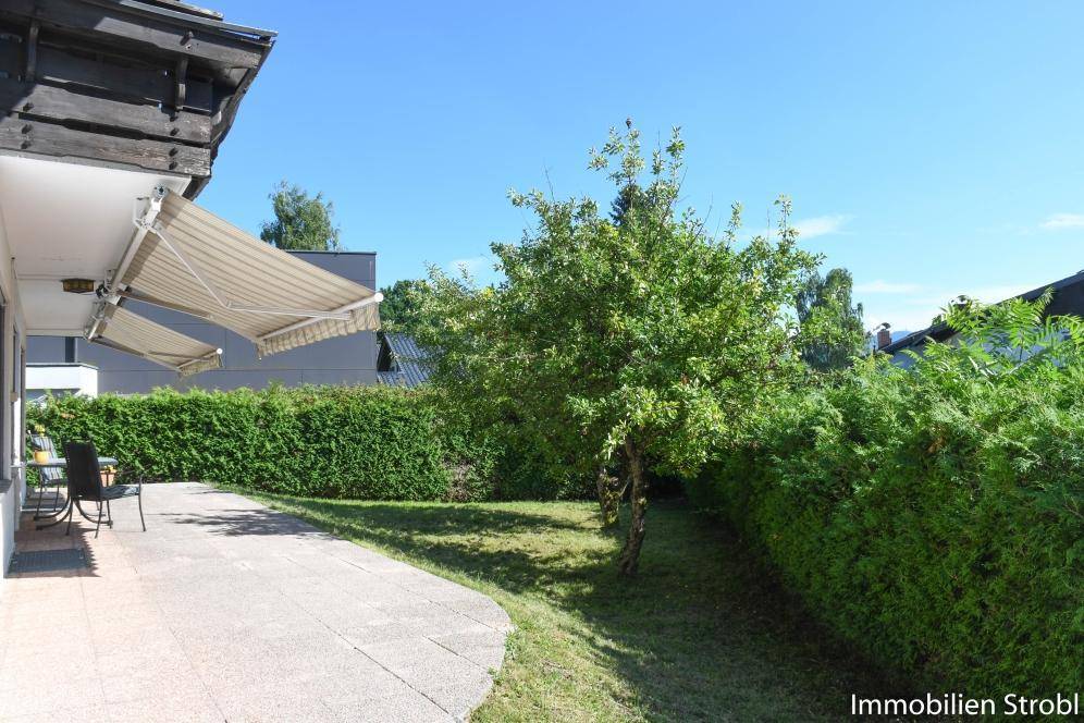 Sonnige Terrasse mit ausfahrbarer Markise, umgeben von einem gepflegten Garten und grünen Hecken.