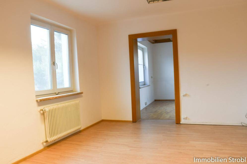 Leerer Raum mit Laminatboden, weißen Wänden und einem Durchgang zu einem weiteren Zimmer.