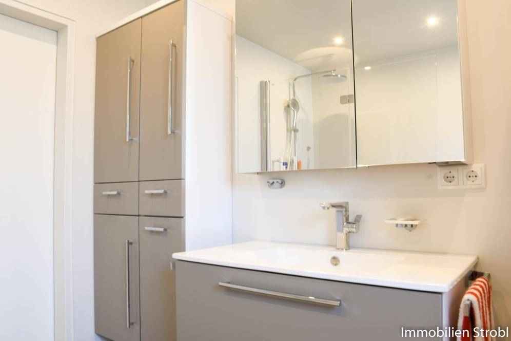 Modernes Badezimmer mit Einzelwaschbecken, Spiegelschrank und begehbarer Dusche.