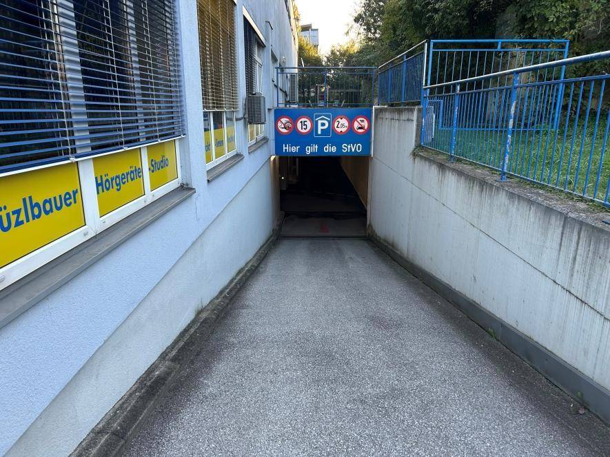 Einfahrt zur Tiefgarage mit Rampe, Hinweisschildern und angrenzendem Gebäude.