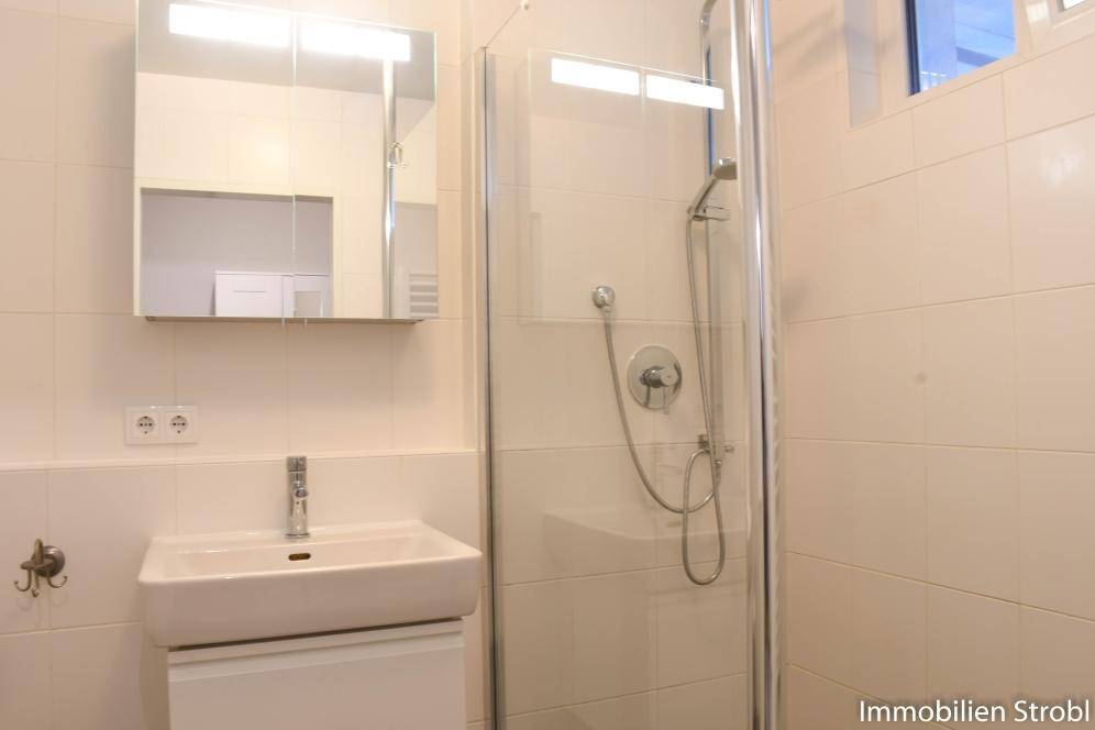 Funktionales Badezimmer mit Duschkabine, Waschbecken, Spiegelschrank und hellen Fliesen.