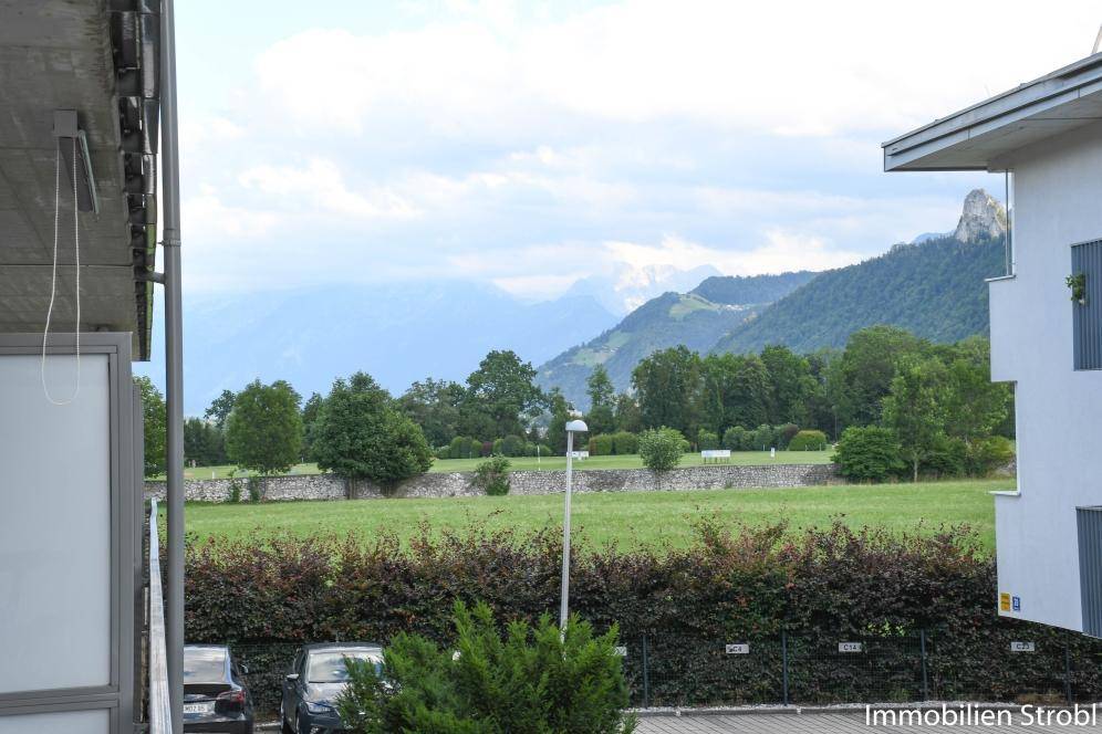 Weitläufiger Blick von einem Balkon auf grüne Felder, Bäume und die majestätische Berglandschaft.