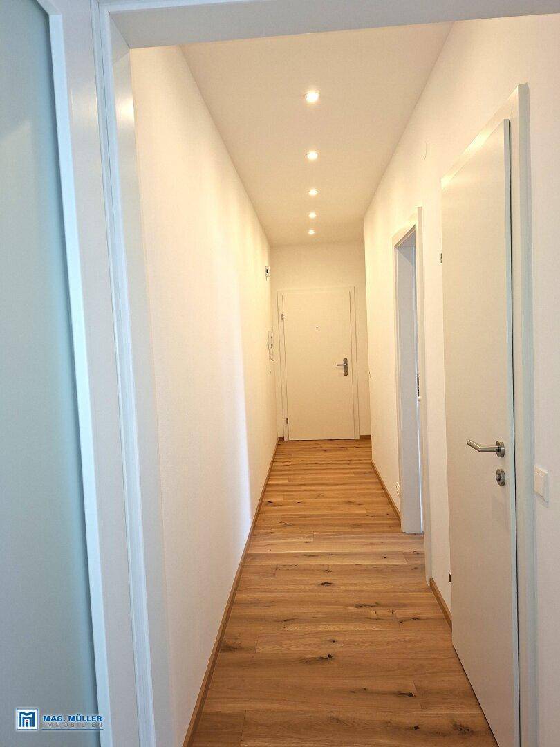 Heller Flur mit Holzboden und Einbaustrahlern, der zu weiteren Räumen führt.