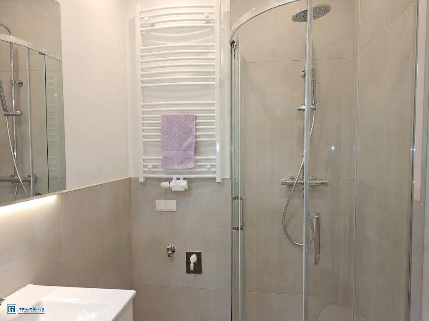 Modernes Badezimmer mit begehbarer Dusche, beheiztem Handtuchhalter und hellen Fliesen.