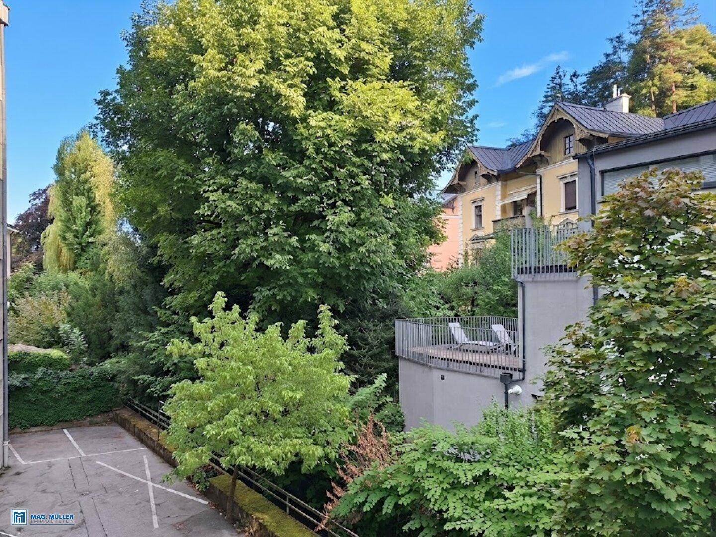 Außenterrasse mit Liegestühlen, umgeben von üppigem Grün und Bäumen.