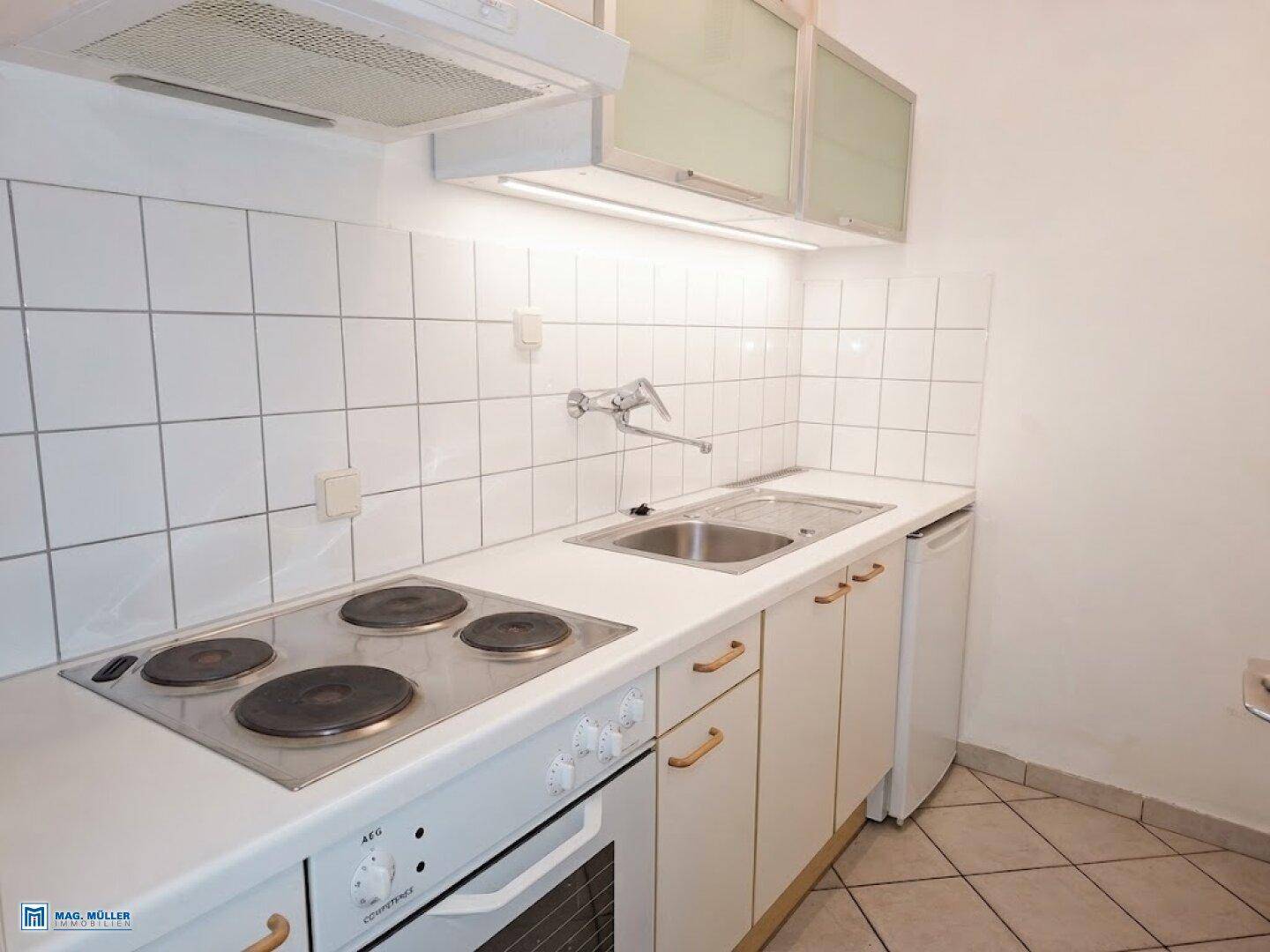 Kleine Küche mit weiß gefliestem Fliesenspiegel, Elektroherd und Spülbecken.