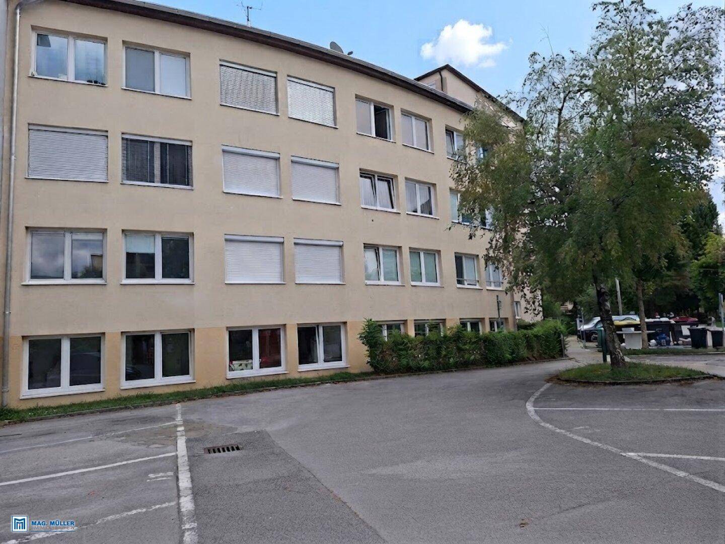 Mehrfamilienhaus mit beiger Fassade, vielen Fenstern und Jalousien.