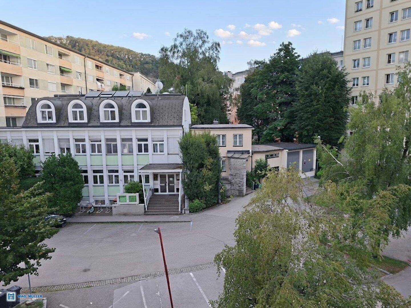 Weitläufiger Blick auf mehrere Gebäude, Bäume und einen Parkplatz.