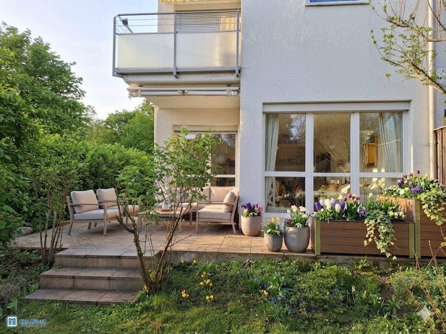 Gemütliche Außenterrasse mit Sitzgelegenheiten und einem Balkon darüber, umgeben von üppigem Grün.