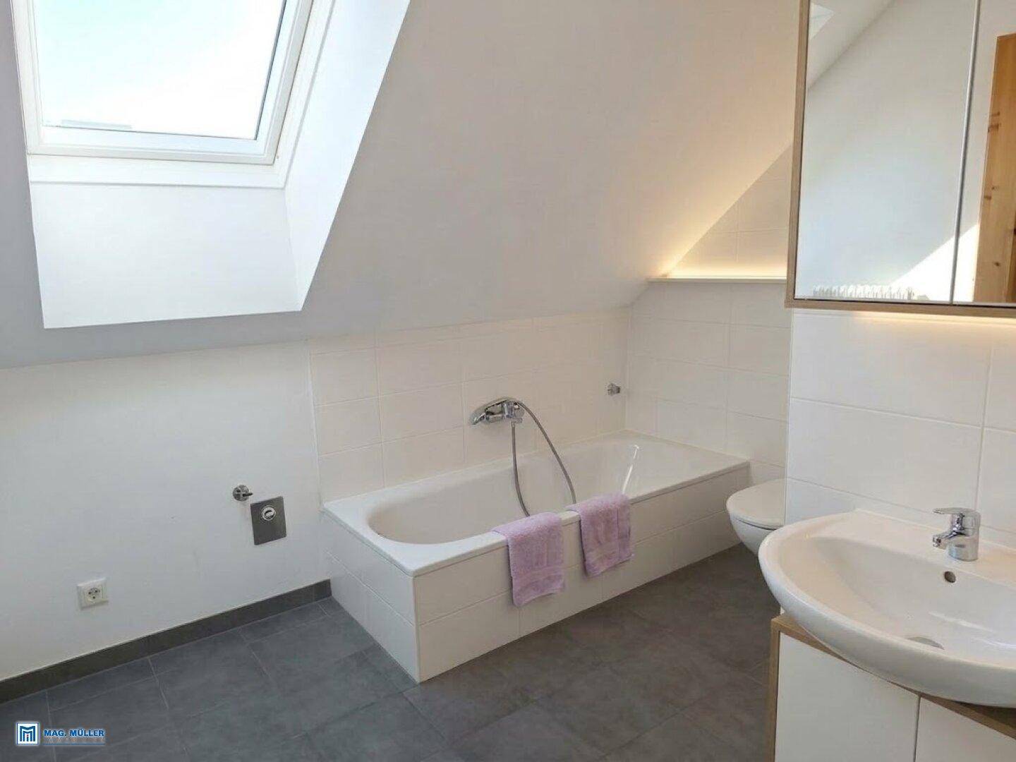 Modernes Badezimmer im Dachgeschoss mit Badewanne, Waschbecken und Dachfenster für Tageslicht.