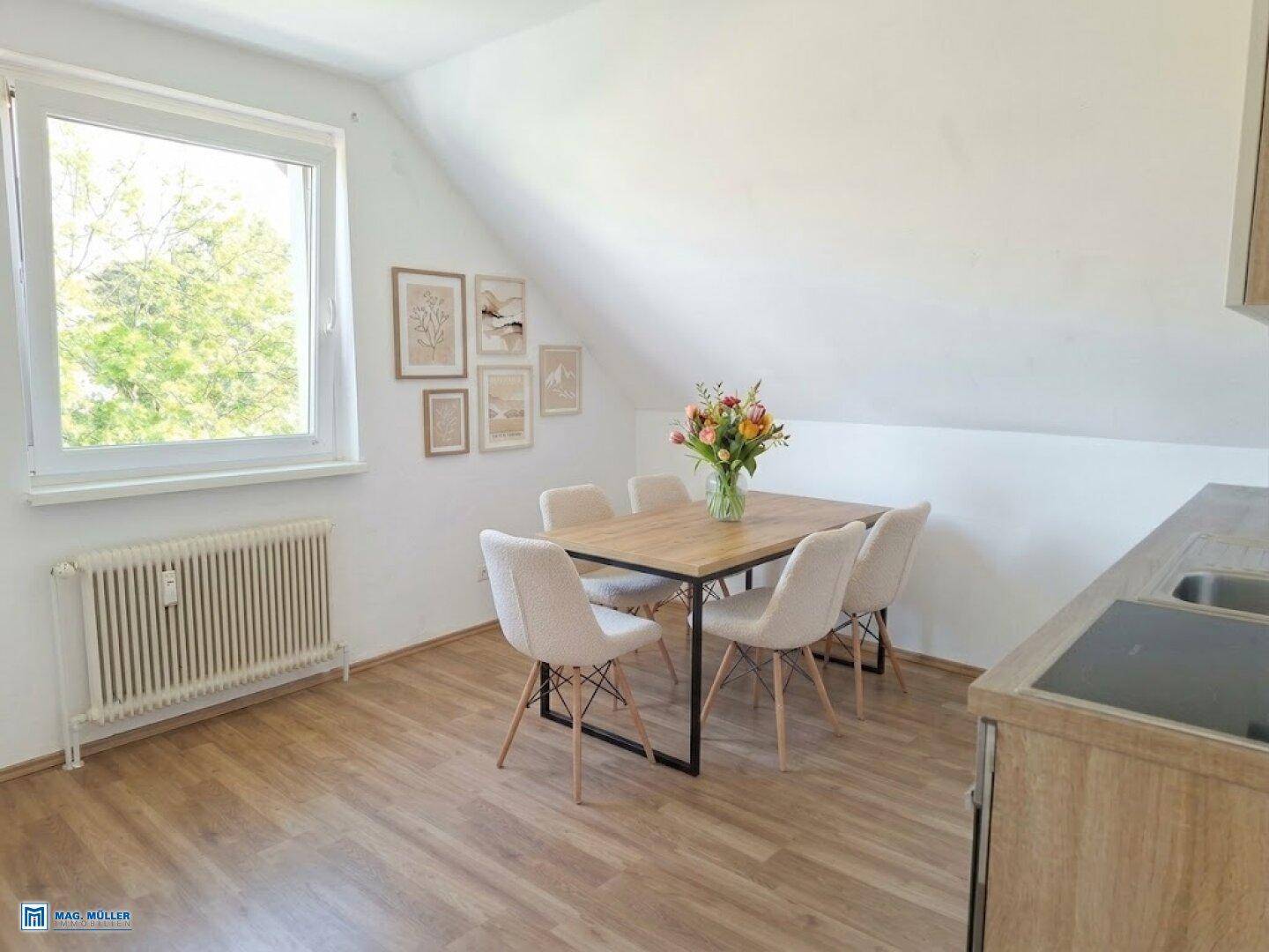 Essbereich in der Küche mit Holztisch, modernen Stühlen und Fenster im Dachgeschoss.