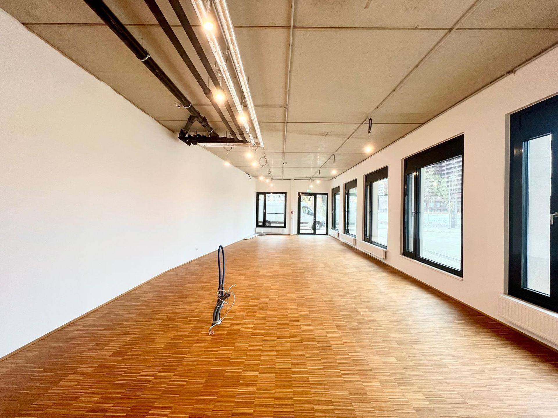 Heller und weitläufiger Gewerberaum mit großen Fenstern und Holzboden in einem modernen Neubau.