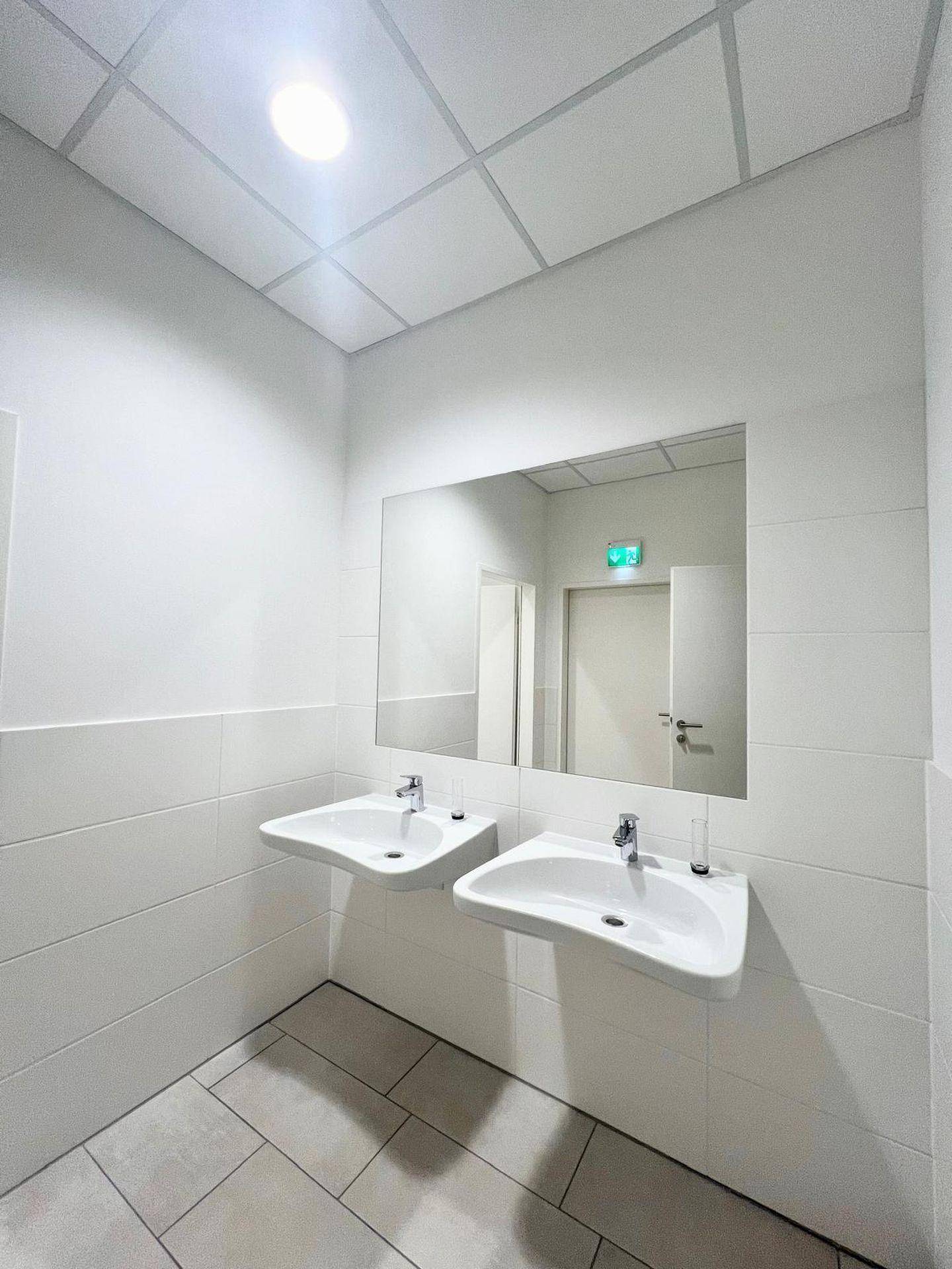 Modernes Badezimmer mit zwei Waschbecken, großem Spiegel und weißen Fliesen an Wänden und Boden.