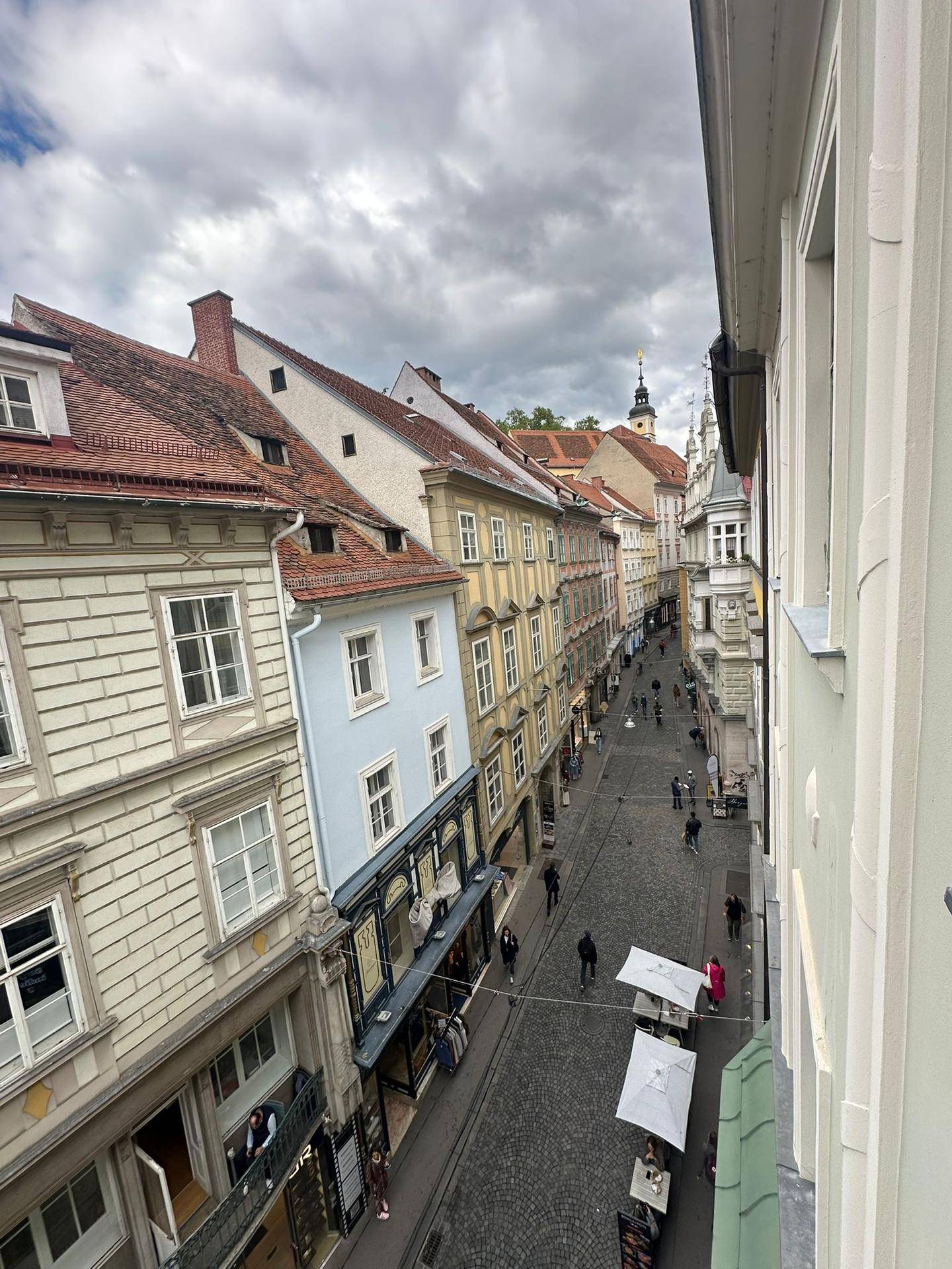 Panoramablick auf eine historische Gasse mit Kopfsteinpflaster, Geschäften und traditionellen Gebäuden.