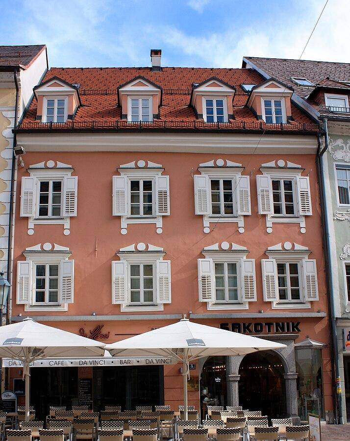 Historisches Gebäude mit lachsfarbener Fassade, roten Dachziegeln und belebter Straßenszene.