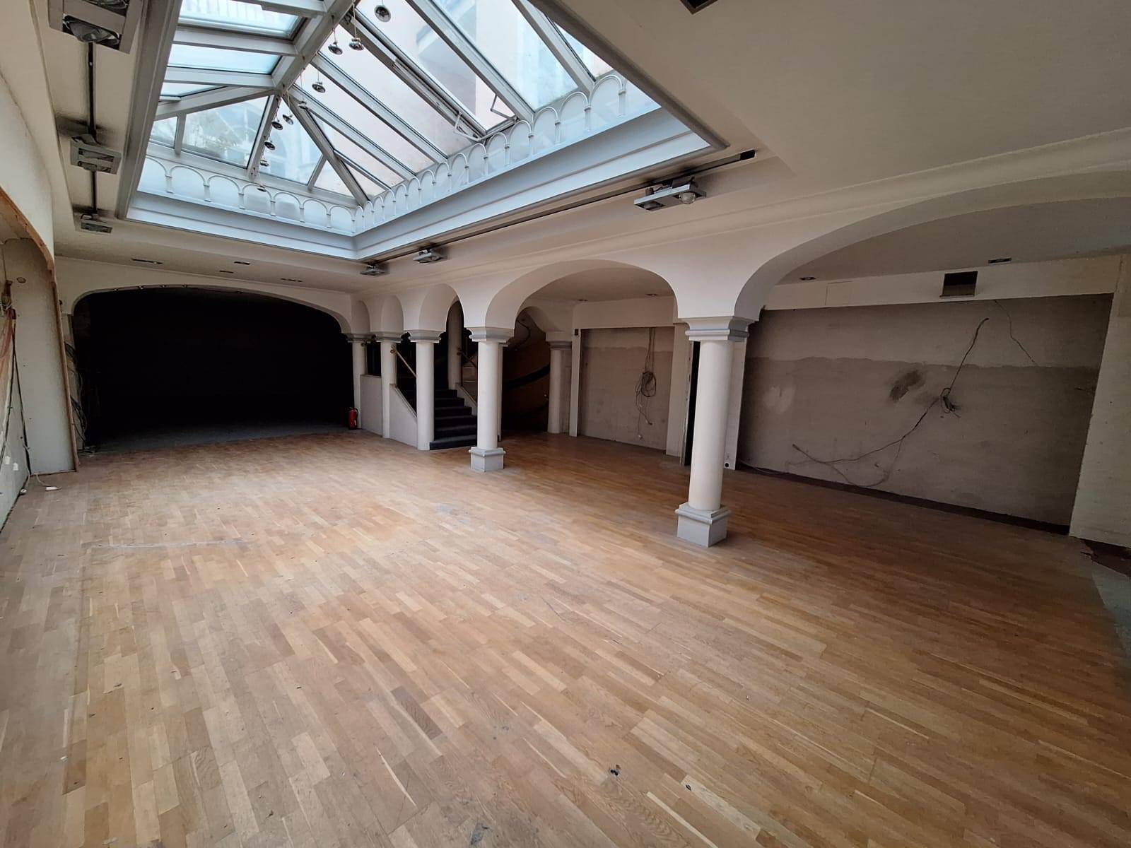 Weitläufiger Gewerberaum mit eleganten Säulen, Holzboden und einem lichtdurchfluteten Glasdach.