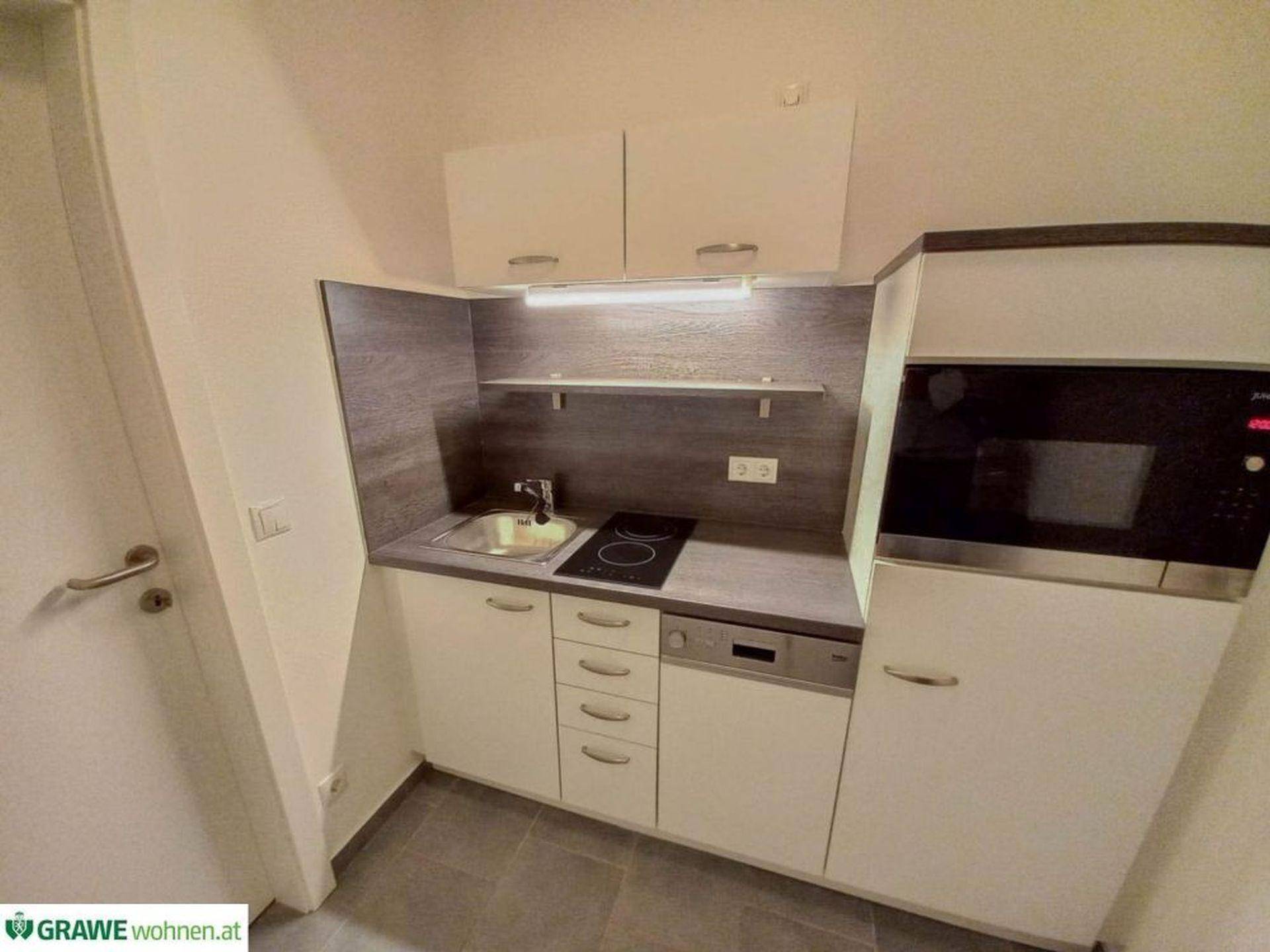Kompakte Küchenzeile mit weißen Schränken, integrierten Geräten und dunkler Arbeitsplatte in modernem Design.