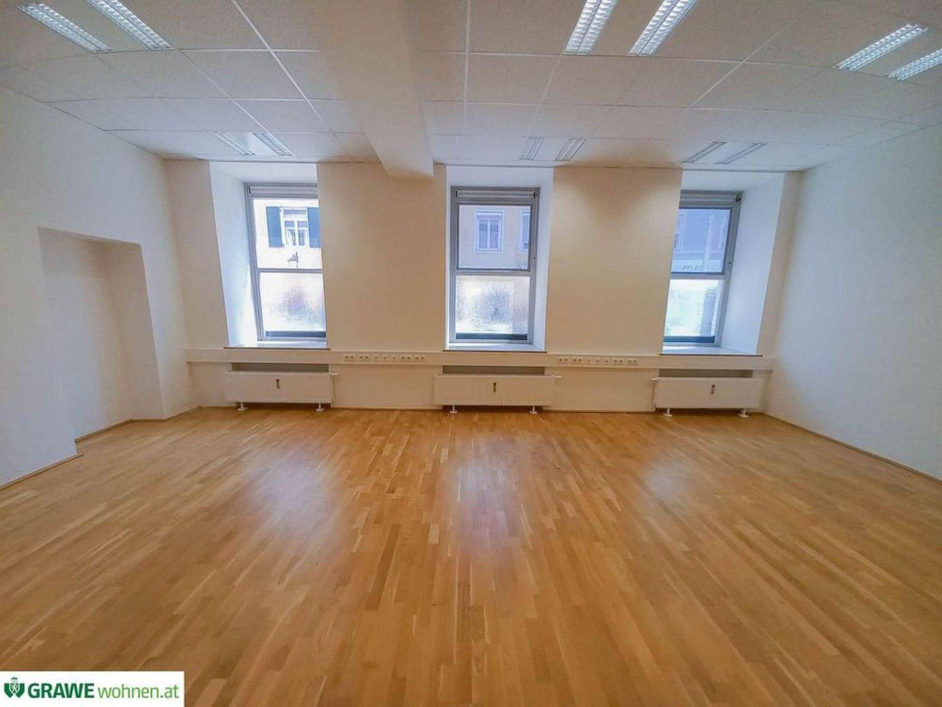 Helles und geräumiges Büro mit vielen Fenstern und einem funktionalen Deckenbeleuchtungssystem.