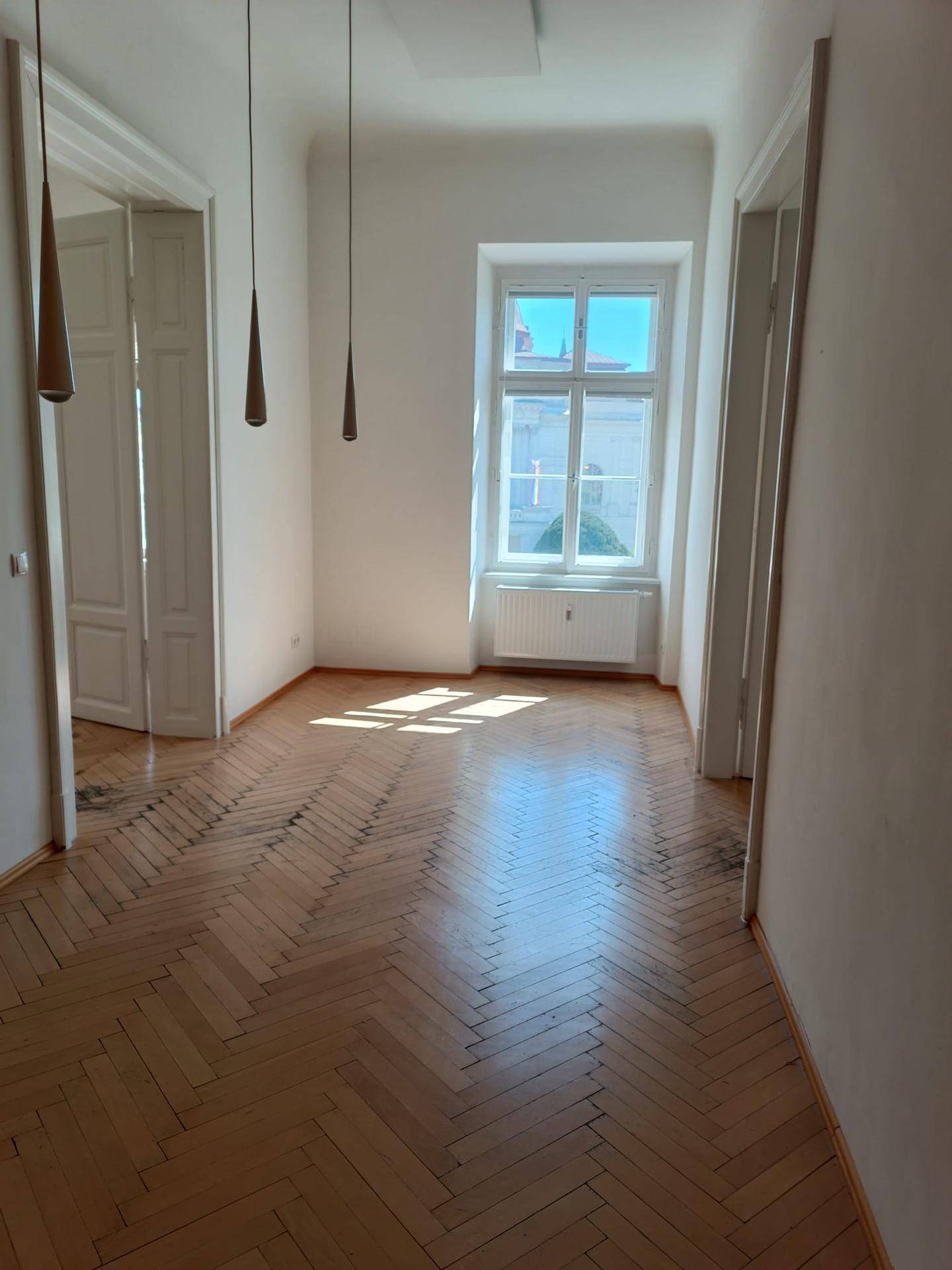 Langer Flur mit klassischem Fischgrätparkett, hohen Decken und einem großen Fenster, das viel Licht spendet.