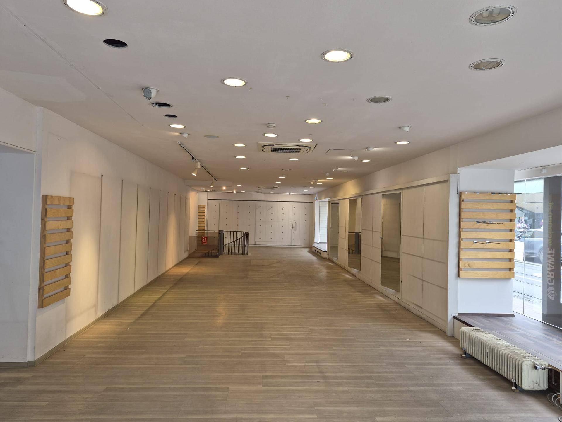Breiter, leerer Gewerberaum mit hellem Holzfußboden und moderner Deckenbeleuchtung.