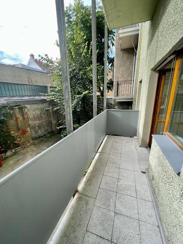Schmaler Balkon mit Fliesenboden und Blick auf die umliegenden Gebäude und Bäume.