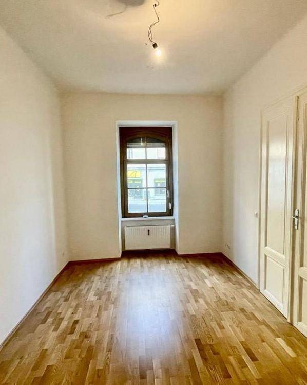 Helles Schlafzimmer mit Parkettboden, großem Fenster und weiß gestrichenen Wänden.