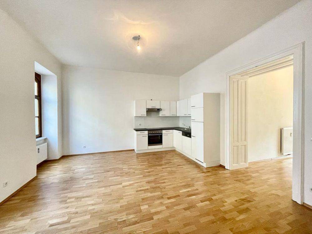 Geräumiger Wohnbereich mit integrierter Küchenzeile, Parkettboden und hohen Decken.