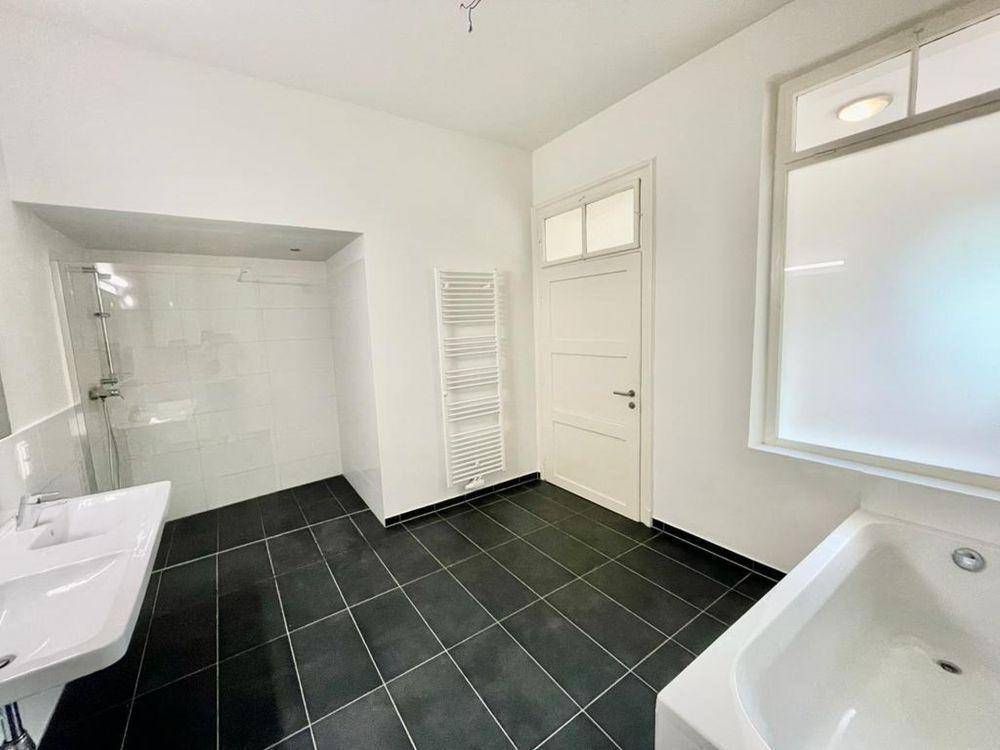 Modernes Badezimmer mit dunklen Fliesen, Badewanne, Dusche und beheiztem Handtuchhalter.