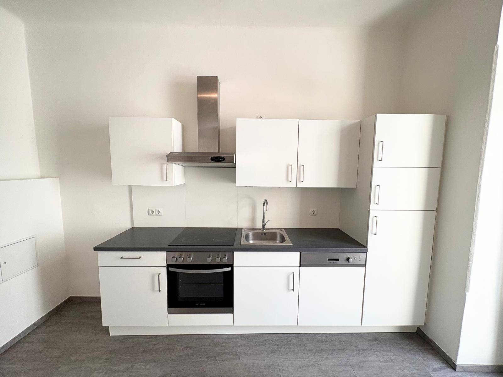 Moderne Einbauküche mit weißen Schränken, dunkler Arbeitsplatte und integrierten Geräten.