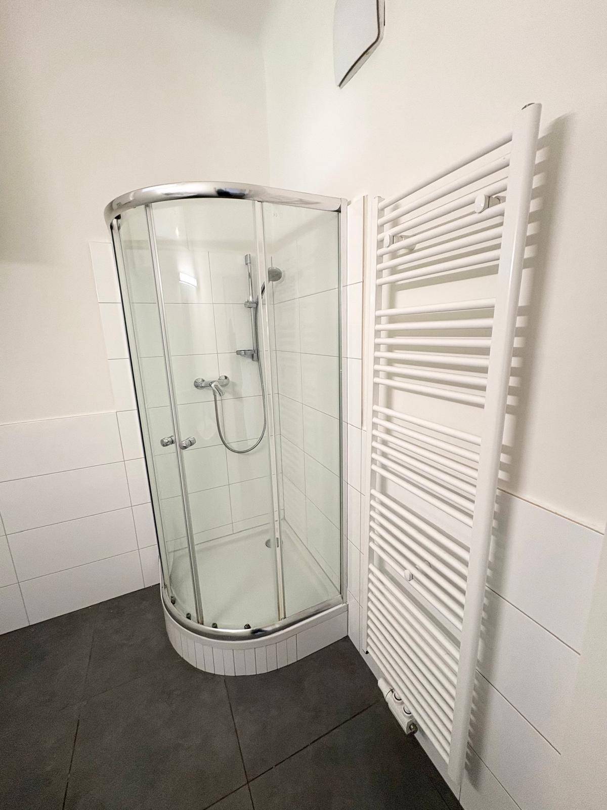 Detaillierte Ansicht der modernen Eckdusche und des weißen Handtuchheizkörpers im Badezimmer.