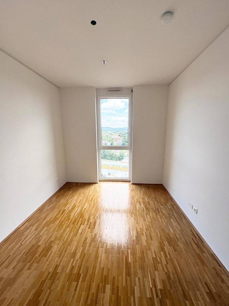 Leeres Zimmer mit Parkettboden und einem hohen Fenster, das einen weiten Blick bietet.