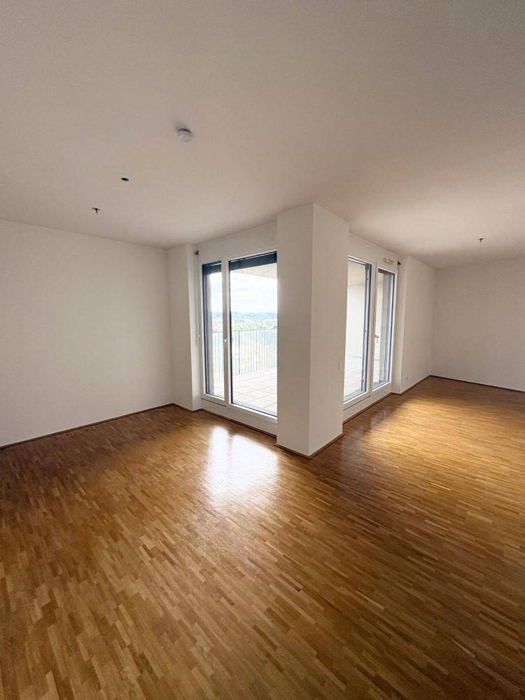 Heller Wohnbereich mit Parkettboden und großen Fenstern, die viel Tageslicht hereinlassen.