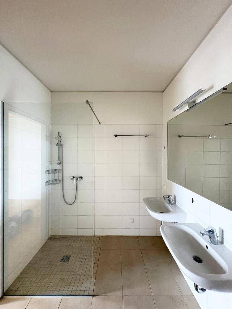 Modernes Badezimmer mit zwei Waschbecken, großer Dusche und hellen Fliesen an den Wänden.